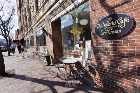 Brick storefronts with large windows and cafe seating on the sidewalk.
