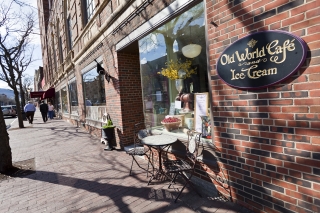 Brick storefronts with large windows and cafe seating on the sidewalk.