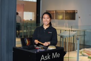 A volunteer smiles while at a kiosk with the words "Ask Me" on it.