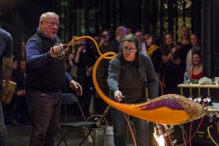 Two gaffers create a swirling tail on an orange and purple oval of molten glass